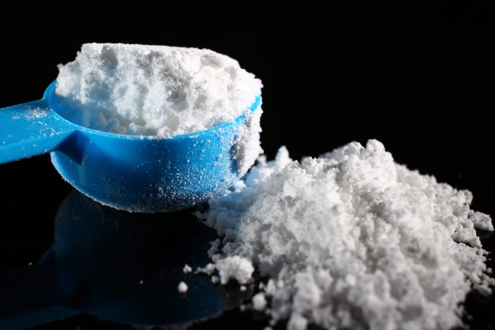 A scoop of white creatine monohydrate powder on a dark surface