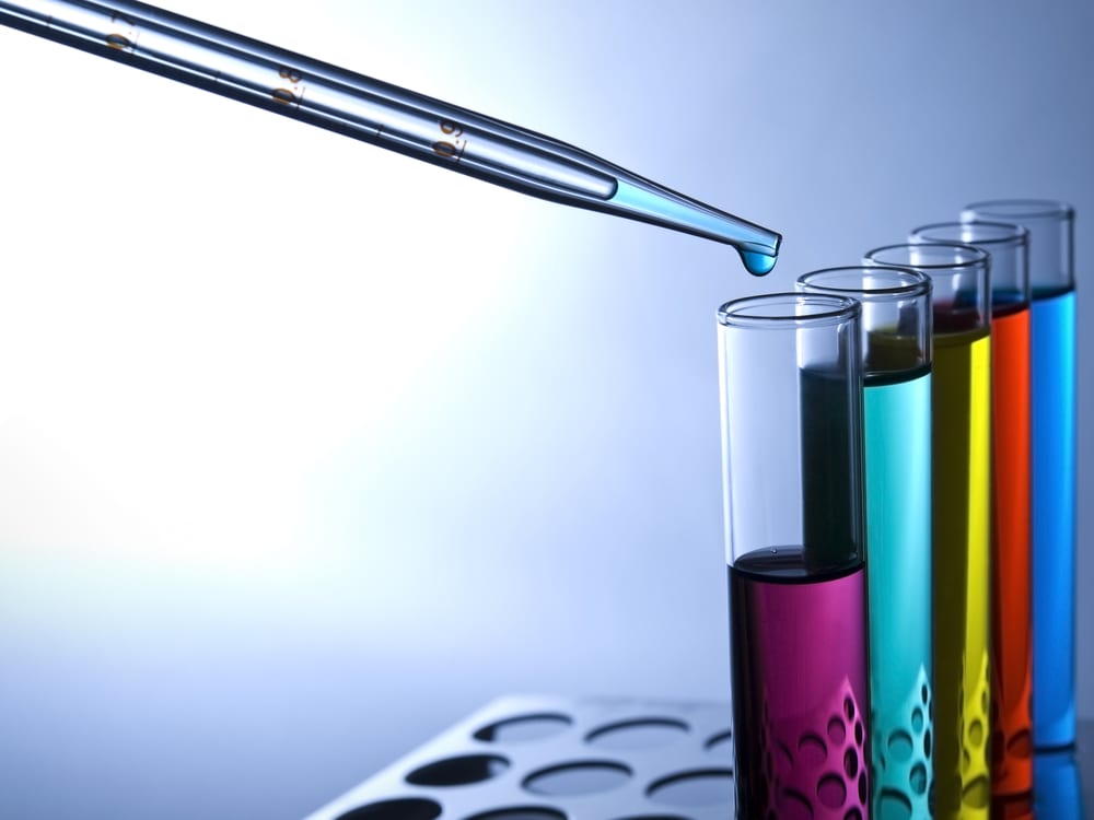 A pipette dropping liquid into colorful test tubes in a flavor lab