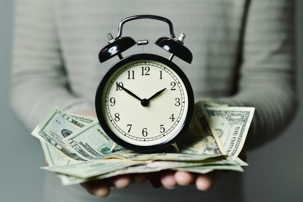 Hands holding a clock over cash, representing time and cost savings