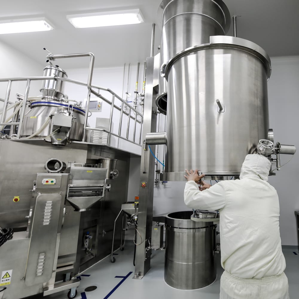 Technician operating supplement manufacturing equipment in a clean room
