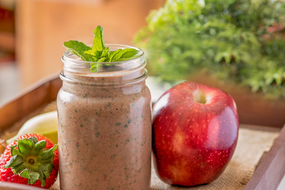 A meal replacement shake in a mason jar surrounded by fresh fruit