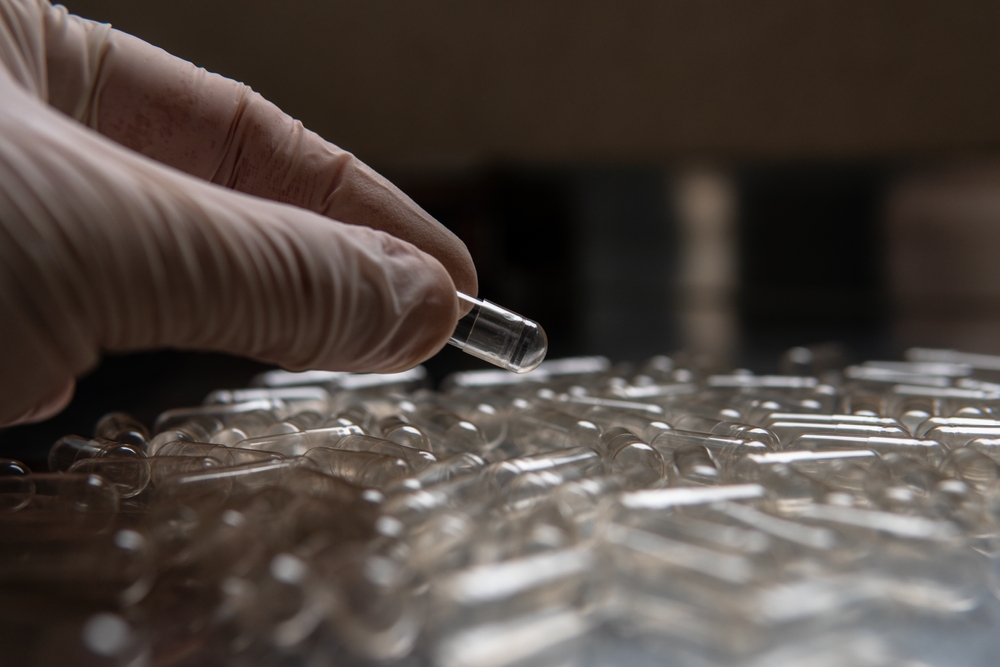Gloved hand inspecting an empty capsule shell during the capsule blend preparation process