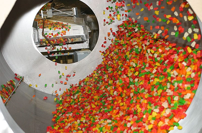 Colorful gummy vitamins tumbling inside a large drum tumbler