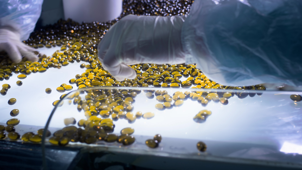 Technicians inspecting softgel capsules for defects on a backlit inspection table